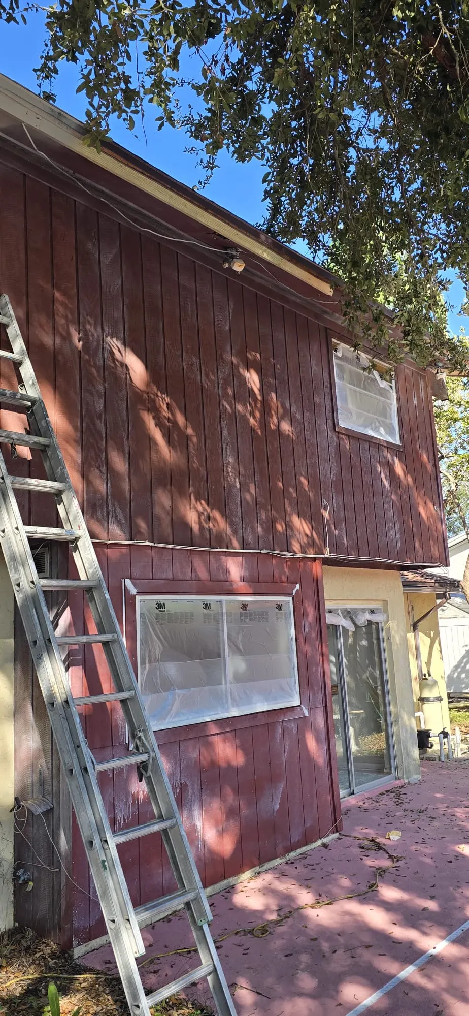 Exterior painting in progress with window masking on a wood siding home
