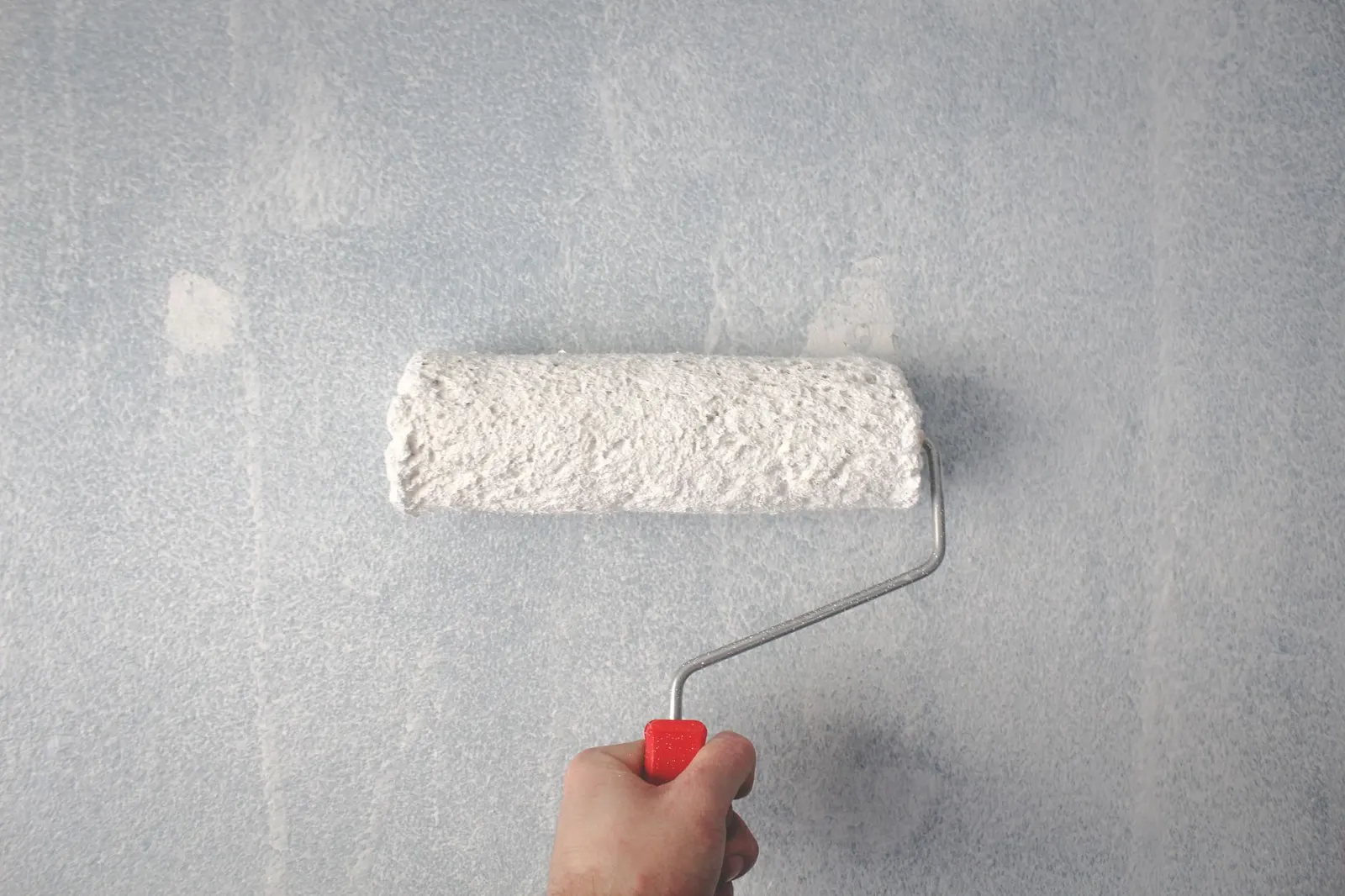 Painter using a roller to apply white paint to an interior wall