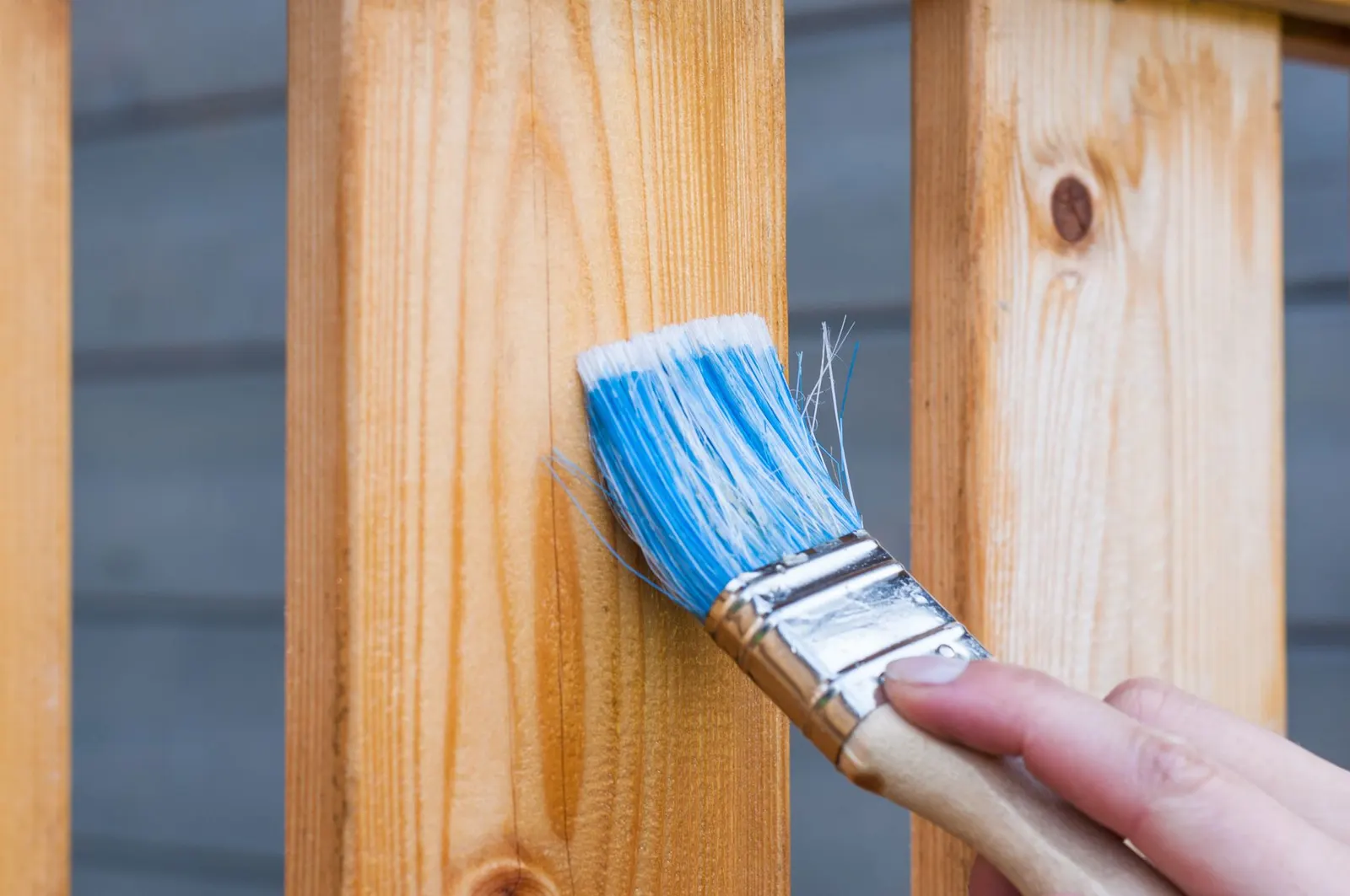 Hand applying stain to a wooden fence with a brush